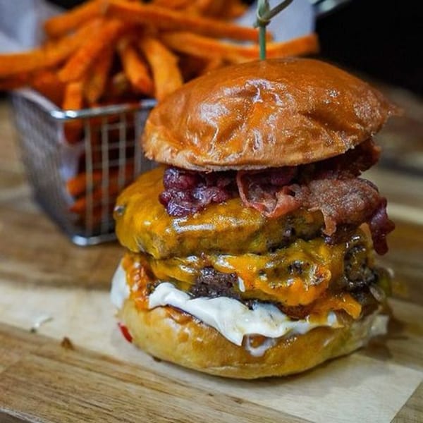 A double cheeseburger with bacon and sauce, served with a side of sweet potato fries.
