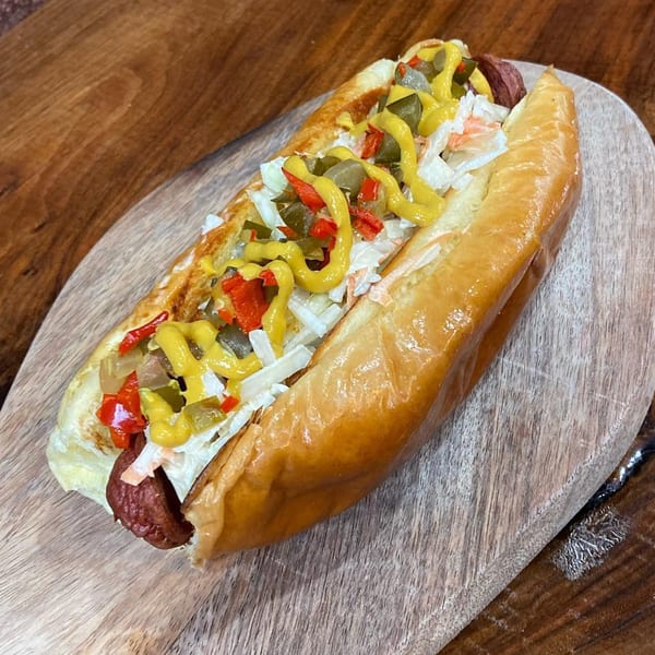 A Sin City Burger hot dog with mustard, relish, and coleslaw on a wooden board.