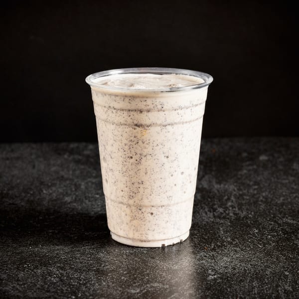 A Sin City Burger cookies and cream milkshake in a clear plastic cup on a dark surface.