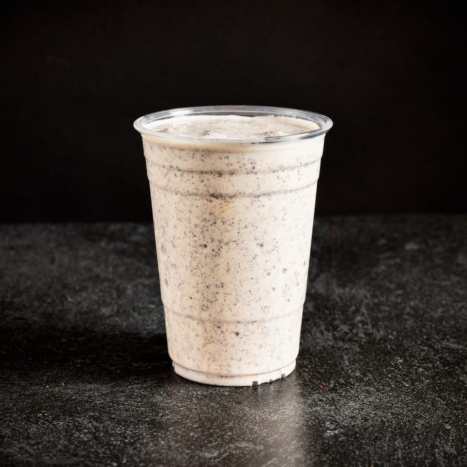 A Sin City Burger cookies and cream milkshake in a clear plastic cup on a dark surface.